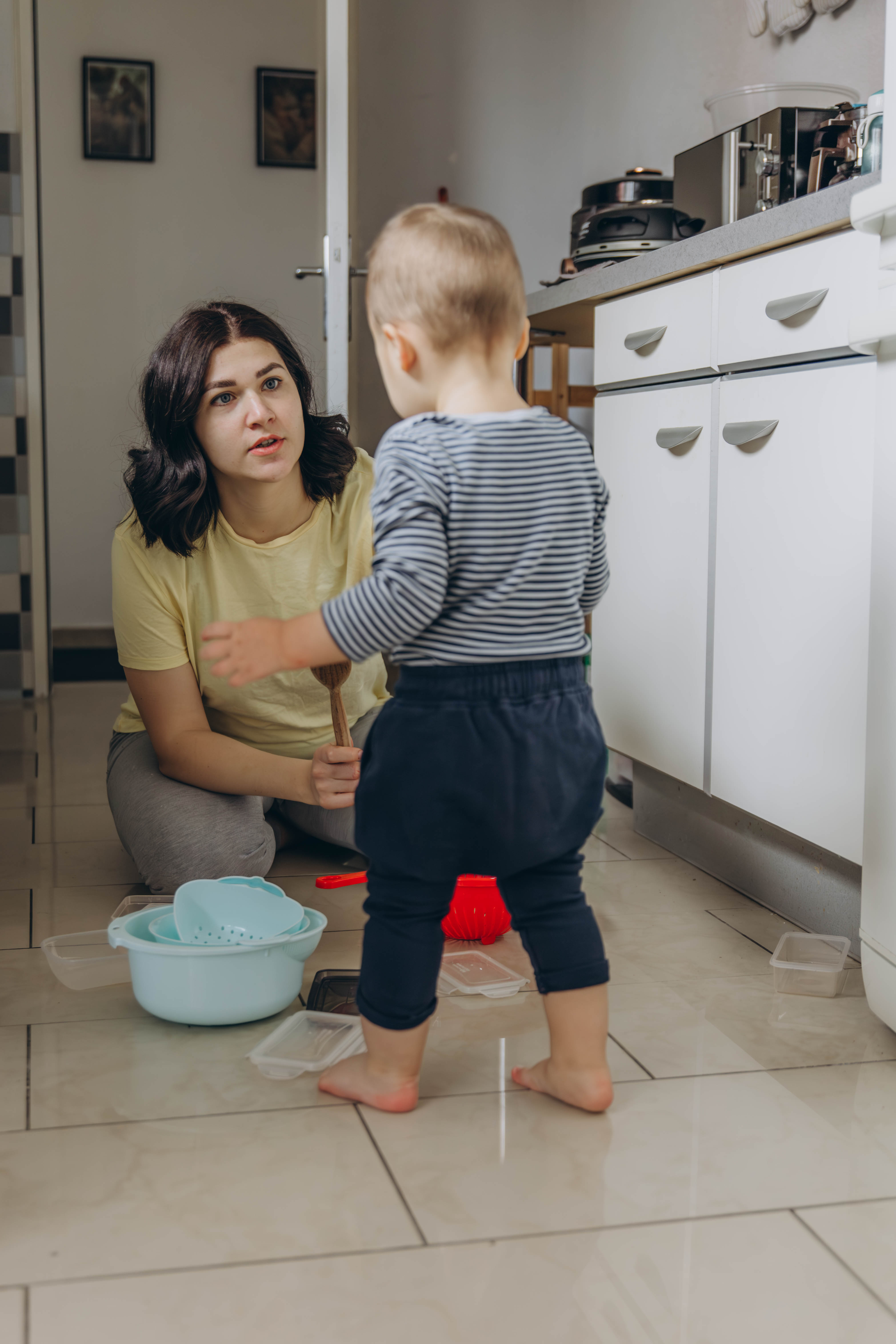 Mother kneeling, talking calmly with her toddler in the kitchen