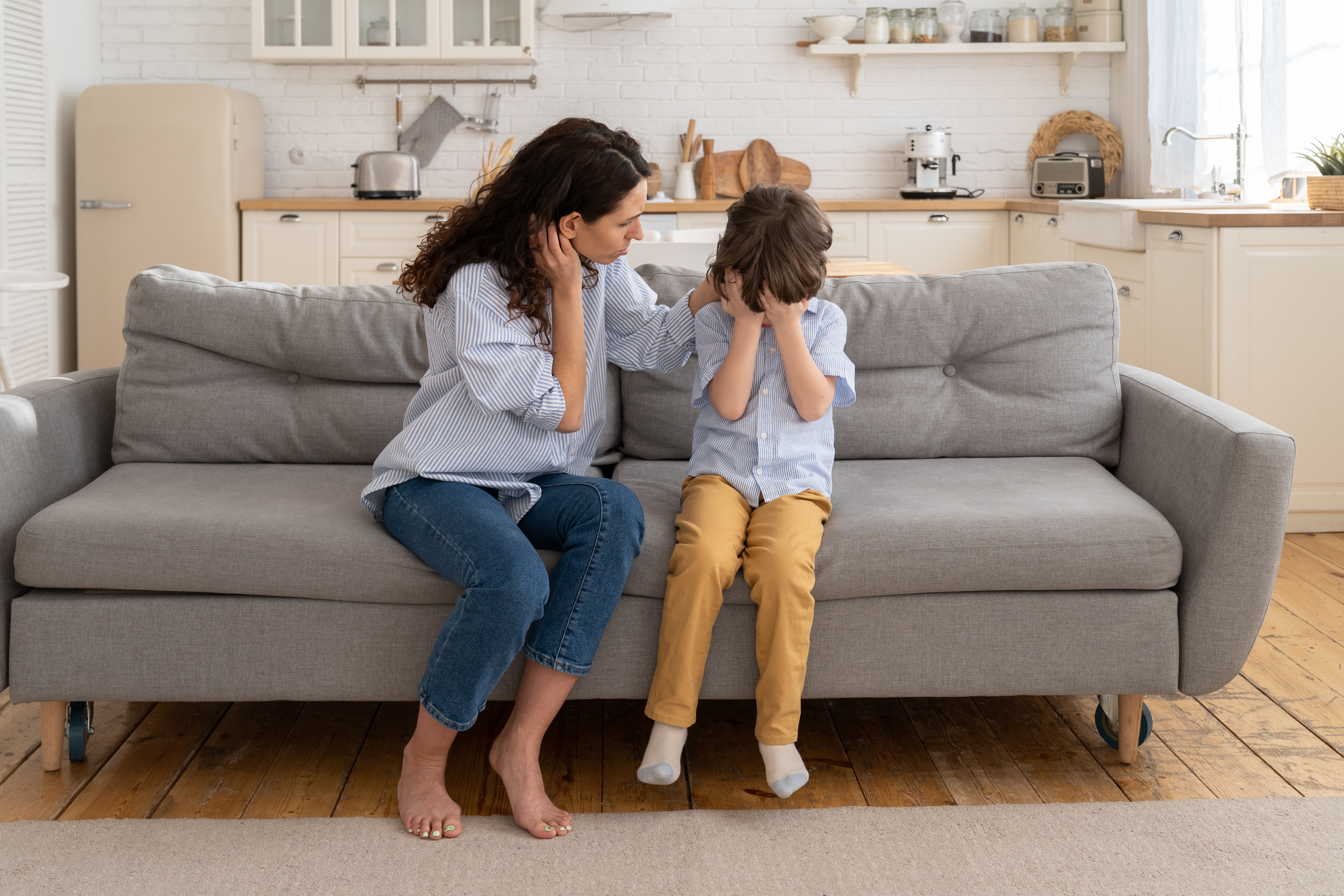 Mother sitting next to her son on the couch as he covers his face